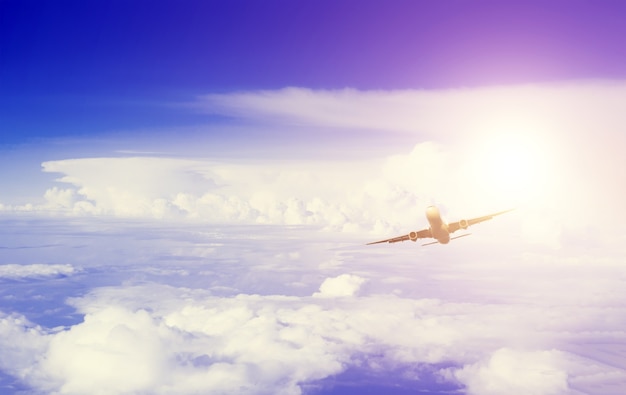 Vista inferior na distância de voar o avião no céu entre as nuvens à tarde