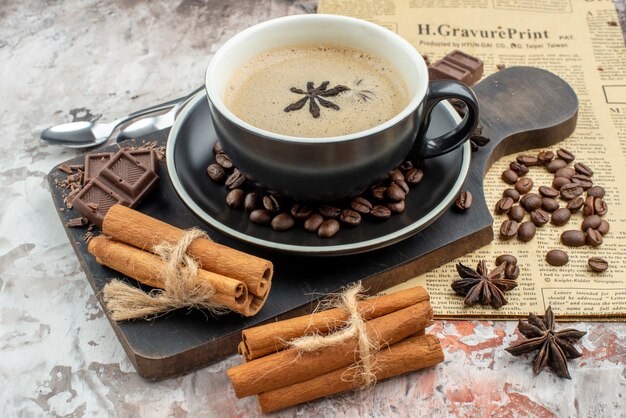 Vista inferior de la taza de café con palitos de canela y chocolate en la placa de madera granos de café tostados en un platillo cucharas de anís periódico en la mesa