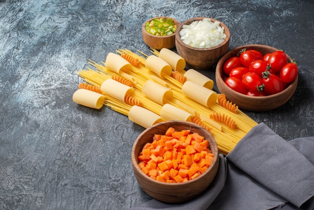 Vista inferior varias pastas rigatoni espaguetis espirales verduras picadas en cuencos de madera sobre fondo gris