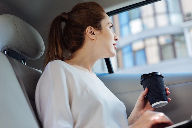 Vista interessante. Mulher agradável e positiva sentada no carro olhando pela janela enquanto aprecia a vista