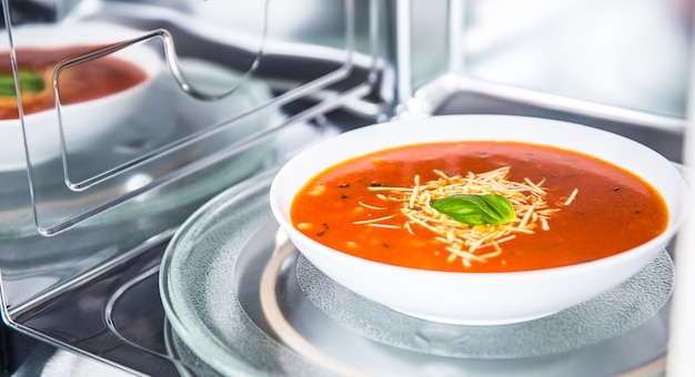 Vista interior del nuevo horno microondas staniless limpio con una sopa de tomate en un plato blanco.