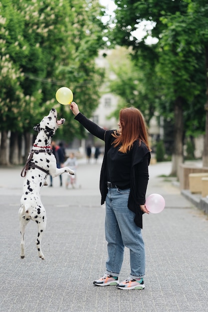 Vista de la joven mujer caucásica jugando y entrenando a su perro dálmata, más tamaño femenino gastar ocio con mascota mejor amigo disfrutando el fin de semana en la calle