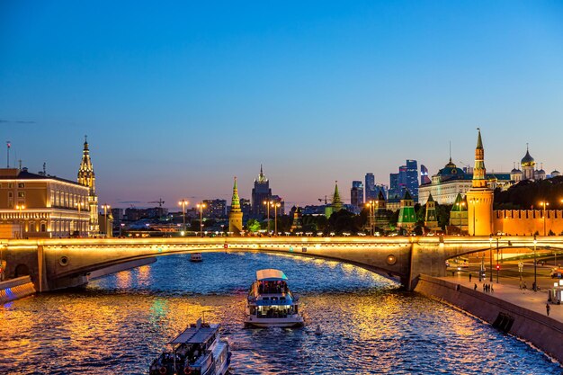 Vista del Kremlin de Moscú y los rascacielos de la ciudad de Moscú a lo largo del muelle del río Moscú con barcos turísticos durante la hora azul del atardecer.