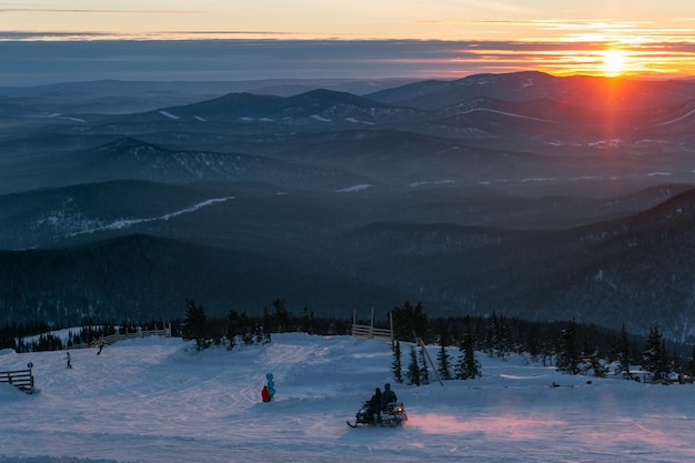 Vista de la ladera de la estación de esquí al atardecer con una moto de nieve