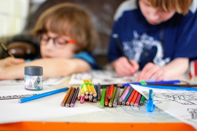 Vista de lápices de colores en la mesa con niños dibujando en el fondo