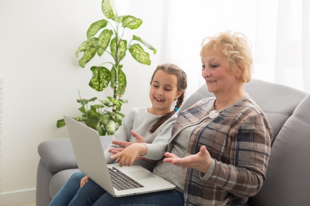 Vista lateral de una abuela y una nieta usando una computadora portátil en la sala de estar en casa