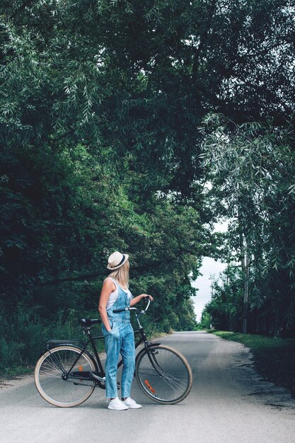 Foto vista lateral de una adolescente con una bicicleta de pie en la carretera