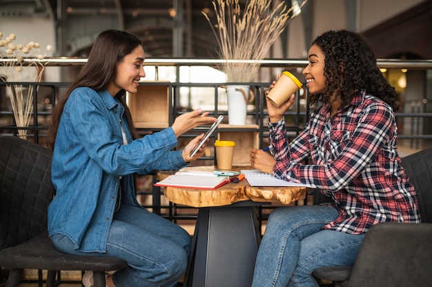 Vista lateral de amigas haciendo los deberes en el café mientras toma una copa