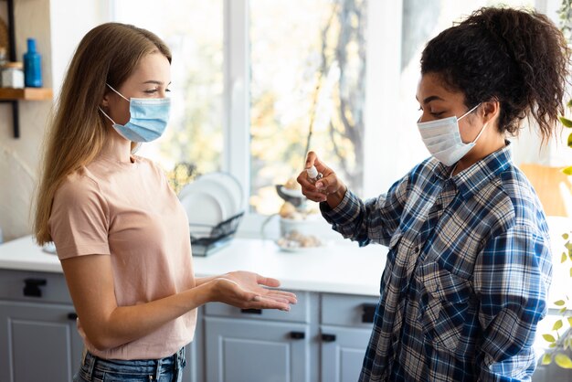 Vista lateral de amigas con máscaras médicas con desinfectante de manos