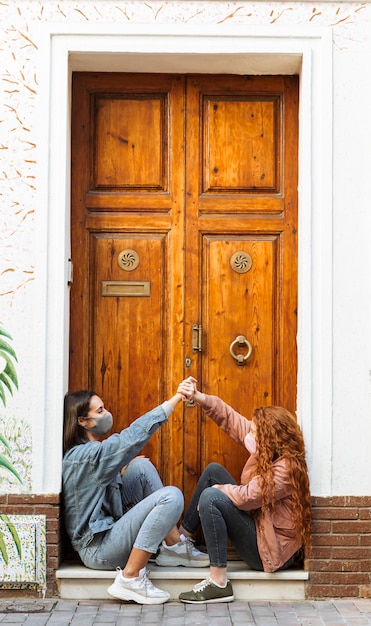 Foto vista lateral de amigas con mascarillas sentado junto a la puerta