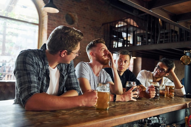 Vista lateral de amigos con cerveza Gente con ropa informal sentada en el pub