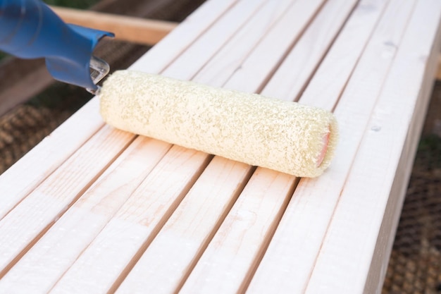 Vista lateral del aplicador de rodillo de pintura blanda blanca para paredes de color y banco de madera con cepillo de piso al aire libre Sitio de construcción