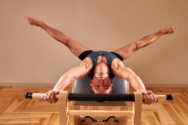 Vista lateral del atleta masculino descalzo acostado en el reformador de pilates y realizando ejercicios abdominales durante el entrenamiento de fitness Concepto de hombre de Pilates