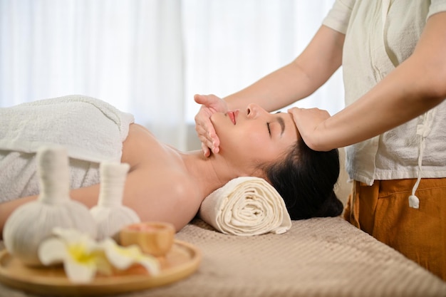 Vista lateral Atractiva mujer asiática ojos cerrados recibiendo tratamiento de masaje facial en el salón de spa