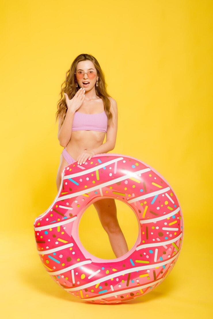 Vista lateral de la atractiva mujer joven en traje de baño gafas de sol de moda con anillo de natación en forma de rosquilla