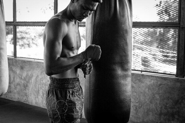 Foto vista lateral de un boxeador sin camisa de pie junto a una bolsa de boxeo en el gimnasio