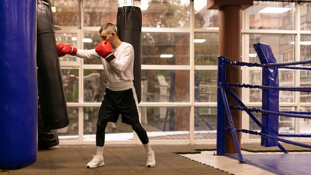 Vista lateral del boxeador masculino practicando con saco de boxeo en el ring