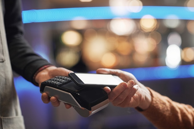 Vista lateral de cerca del hombre irreconocible que paga con tarjeta de crédito, se centran en las manos que sostienen la tarjeta sobre la terminal, copie el espacio