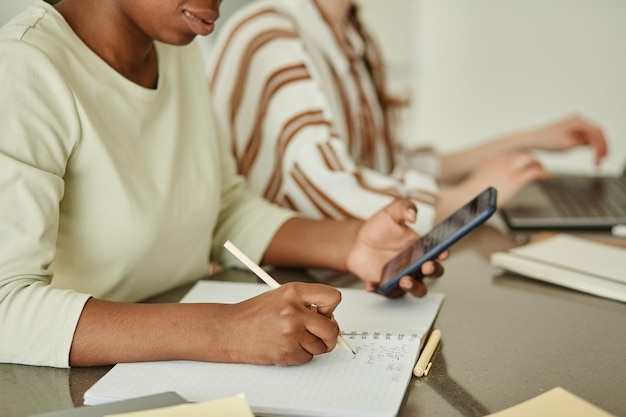 Vista lateral de cerca de una joven negra que sostiene un teléfono inteligente mientras investiga para una pequeña empresa