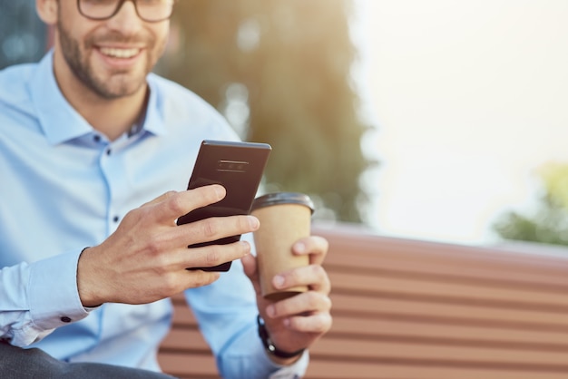 Foto vista lateral de chat en línea de un hombre de negocios feliz con smartphone y tomando café mientras