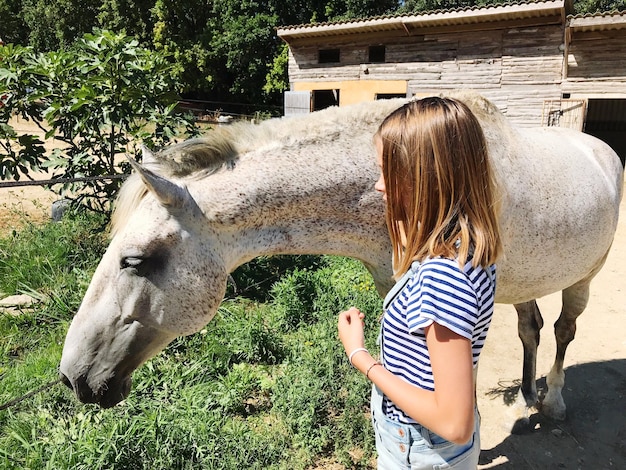 Foto vista lateral de una chica de pie junto al caballo