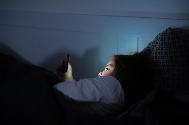 Vista lateral de una chica usando un teléfono inteligente acostada en la cama