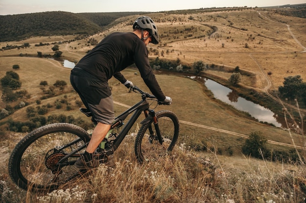 Vista lateral del ciclista masculino irreconocible en ropa deportiva y casco montando bicicleta de grava eléctrica a través de terrenos montañosos mientras practica actividad extrema en la naturaleza de verano