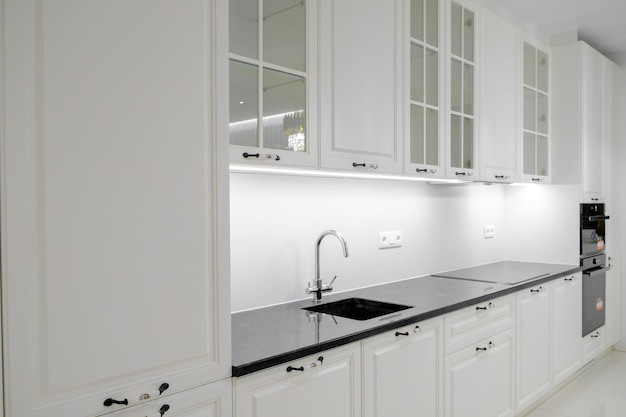 Foto vista lateral cocina moderna y elegante con cajones y armarios blancos, encimera de mármol negro y fregadero incorporado con grifo plateado