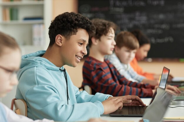 Vista lateral del colegial adolescente que usa la computadora en el aula de la escuela