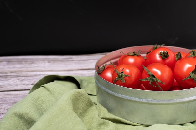 Vista lateral de un conjunto de tomates cherry en recipiente de metal con tela verde