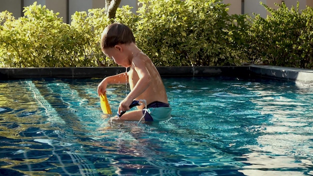 Vista lateral criança molhada em calções de banho tomando banho na piscina com água azul claro em dia ensolarado