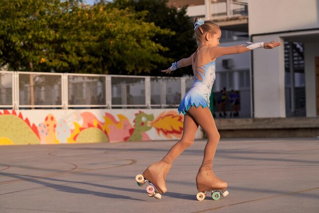 Foto vista lateral de cuerpo completo de una chica deportiva con leotardo colorido montando patines cuádruples mientras entrena en el campo deportivo de la ciudad