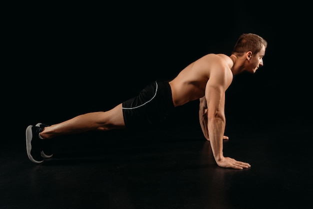 Vista lateral del culturista deportivo muscular haciendo flexiones aislado en negro