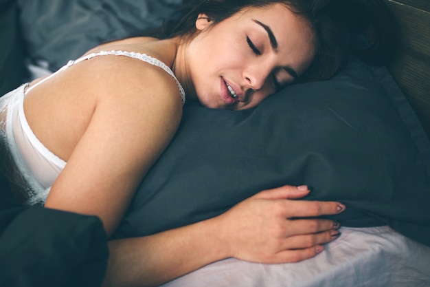 Vista lateral da bela jovem sorrindo enquanto dorme em sua cama em casa