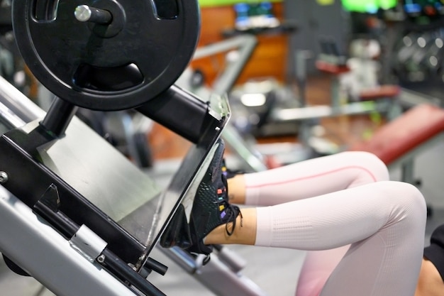 Vista lateral da jovem desportista em forma flexionando os músculos da perna na máquina de exercícios no ginásio.