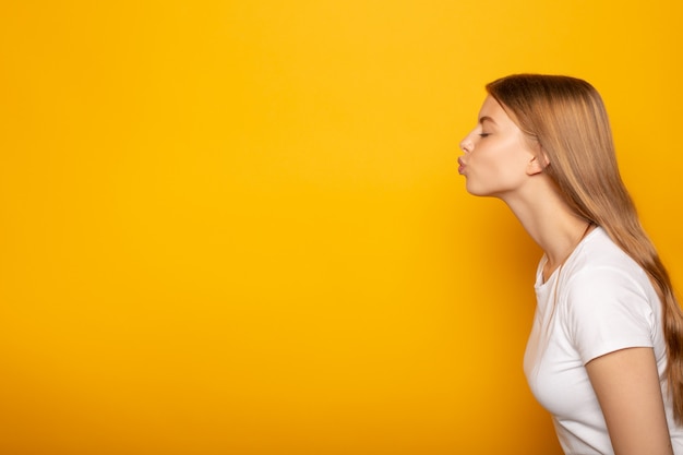 Vista lateral da menina loira beijando com os olhos fechados, isolado no amarelo