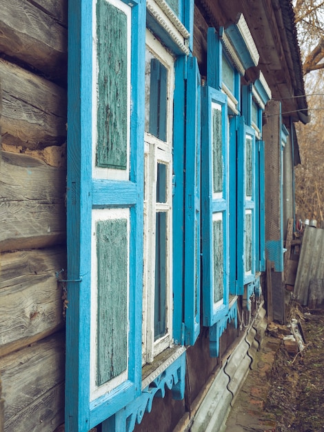 Vista lateral da parede de uma velha casa de madeira com janelas e venezianas azuis. Foco Seletivo