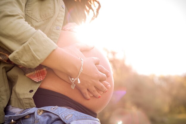 Foto vista lateral da parte média da mulher grávida tocando o estômago durante o dia ensolarado