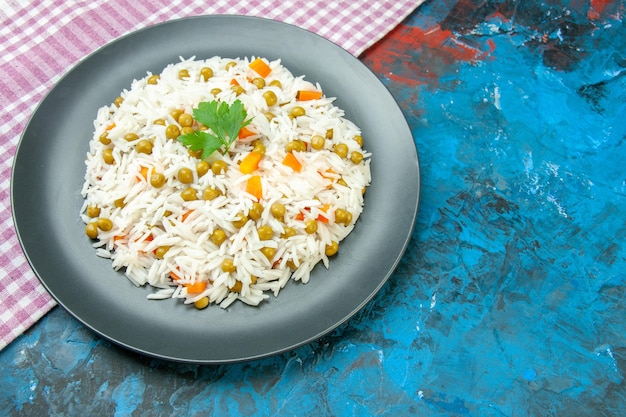 Vista lateral da saborosa refeição de arroz para jantar com cenoura pisum na toalha roxa despojada na mesa azul