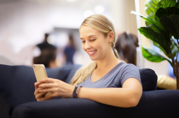 Vista lateral das mulheres olhando no celular com sorrindo enquanto está sentado no sofá