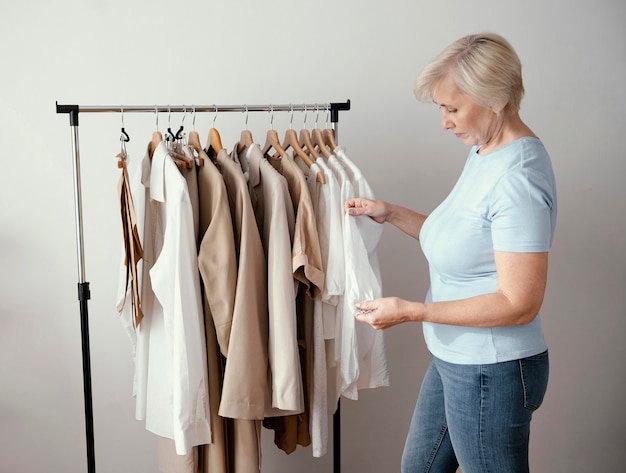 Vista lateral de alfaiate feminina verificando roupas em cabides