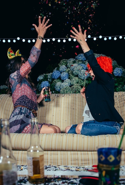 Foto vista lateral de amigas jogando confeti no sofá no pátio durante a noite