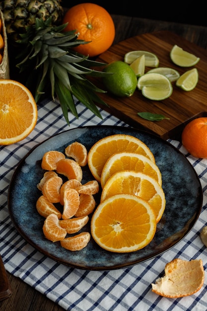 Vista lateral de frutas cítricas como fatias de laranja e tangerina em casca de tangerina prato em pano xadrez inteiro e fatiado de limão na tábua com abacaxi em fundo de madeira