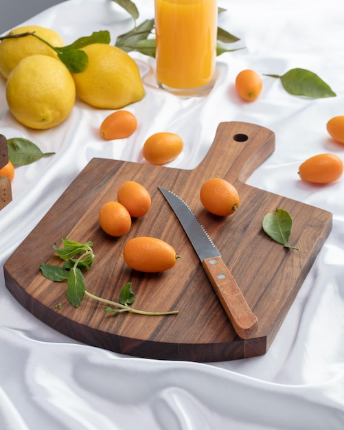 Vista lateral de kumquats com folhas e faca na tábua e limões com suco de laranja em fundo branco