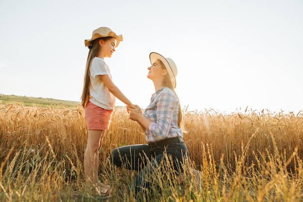 Vista lateral de mãe e filha com chapéu de mãos dadas em criança de campo de trigo dourado e família de mulher ...