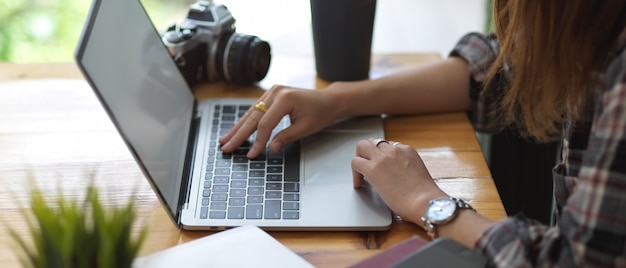 Vista lateral de mãos femininas digitando em um teclado de laptop simulado na mesa de madeira