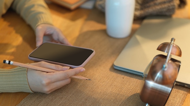 Vista lateral de mãos femininas usando smartphone em uma mesa de trabalho de madeira no escritório doméstico