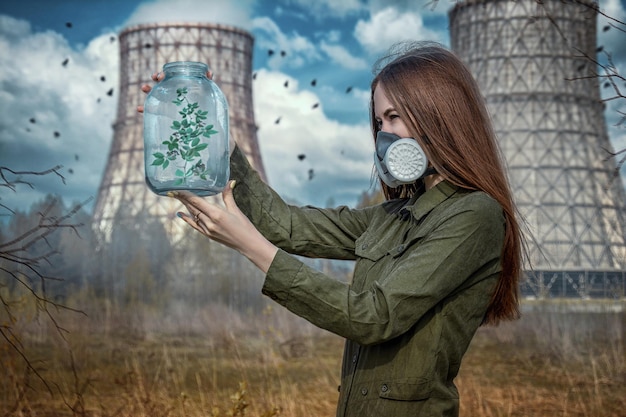 Foto vista lateral de mulher em máscara de gás segurando planta em contêiner enquanto está de pé contra a indústria