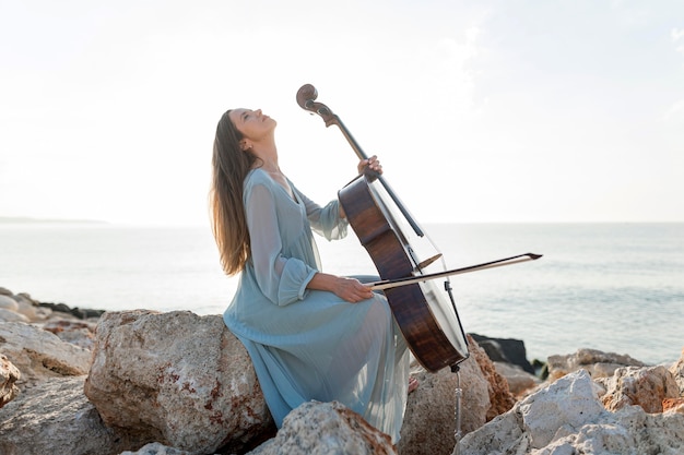 Vista lateral de mulher tocando violoncelo à beira-mar