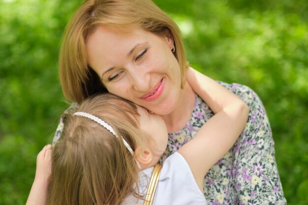 Vista lateral de perto da cabeça feliz filha bonita abraçando abraçando mãe conceito de família feliz retrato de criança sorridente feliz abraçando a mãe em um dia de verão